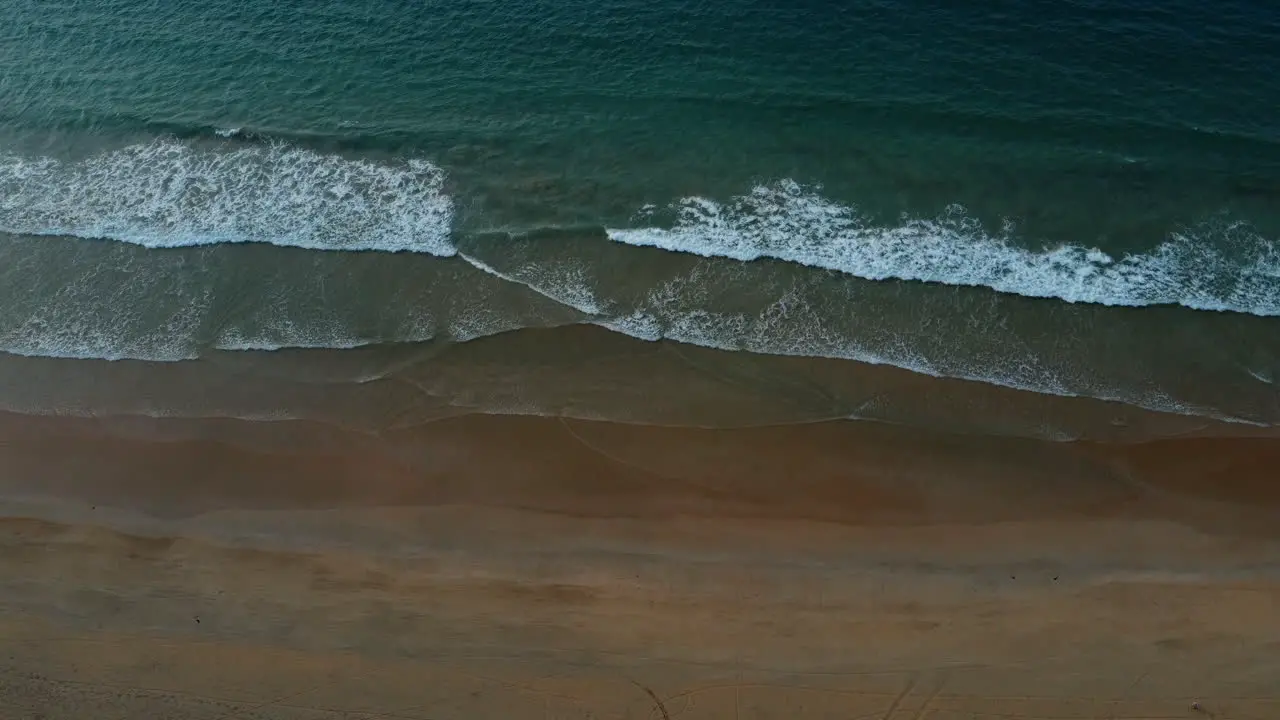 Aerial drone shot of ocean waves crashing on sandy beach