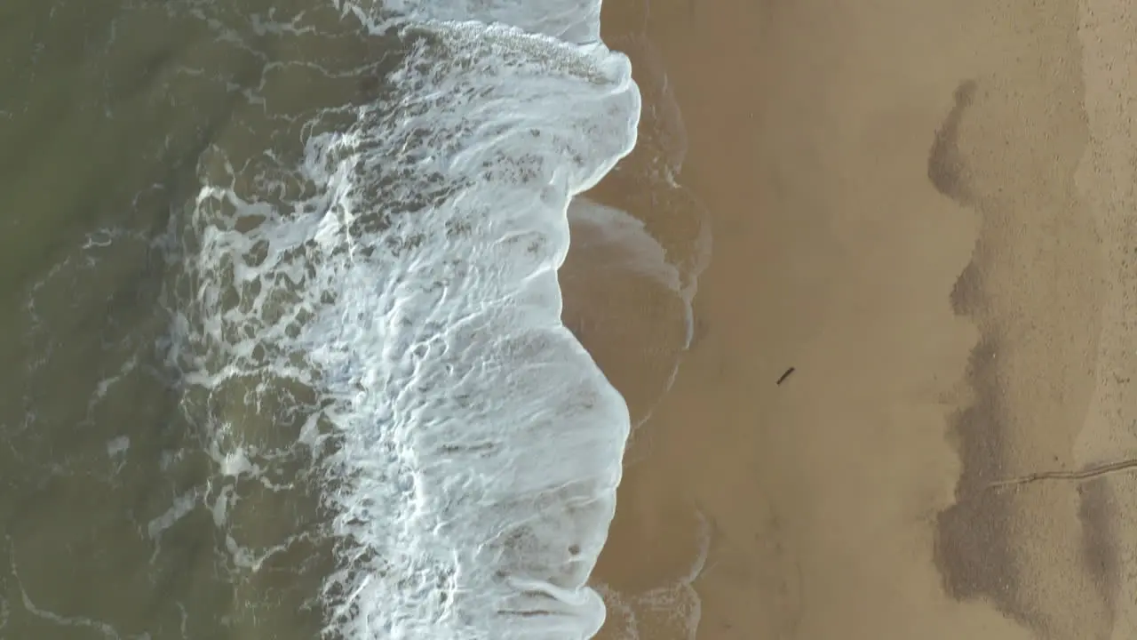 Aerial shot following the crashing waves on a empty sandy golden beach