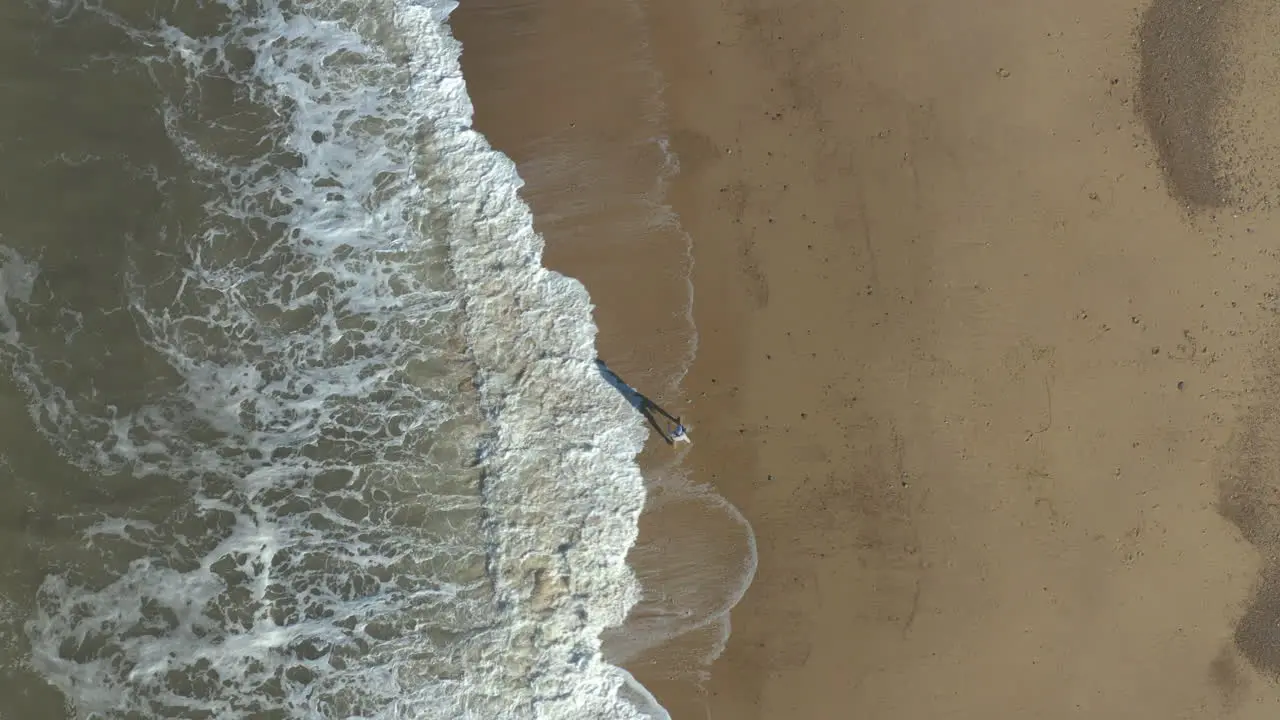 Parent and child having a stroll on an empty beach with big waves crashing at their feet