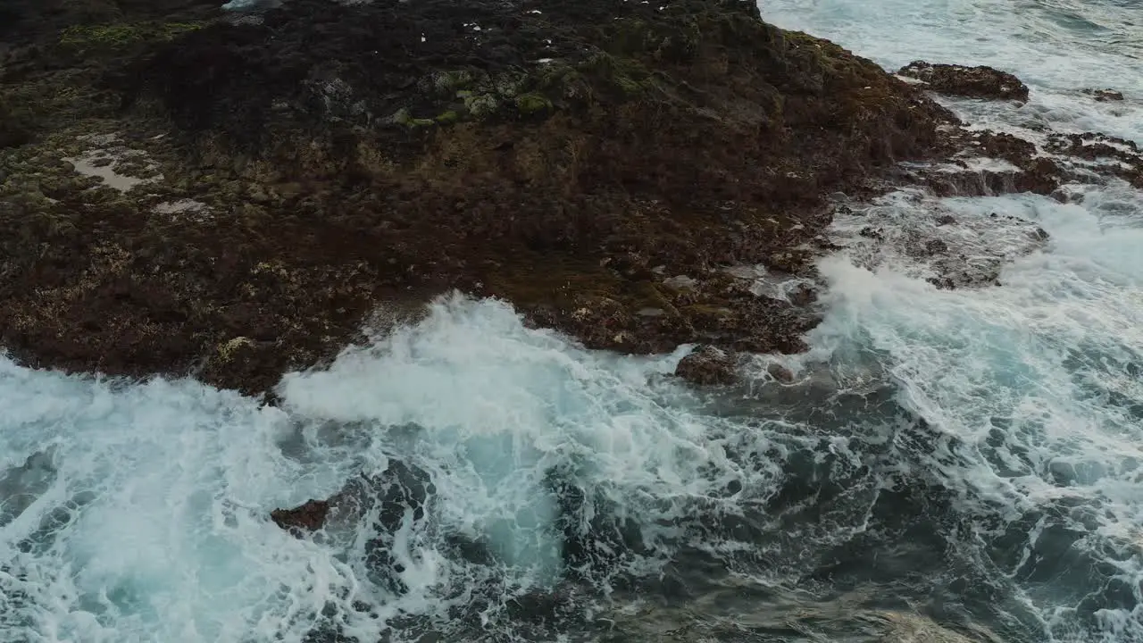 Close drone shot of waves splashing on the coast of an ocean