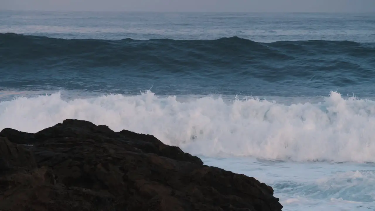 Blue waves roll into the coast of Hawaii in slow motion and break over rocks