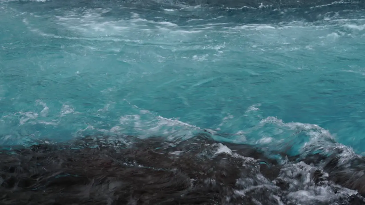 Powerful blue clear water of river flowing between shoreline of Iceland during daytime close up panning shot