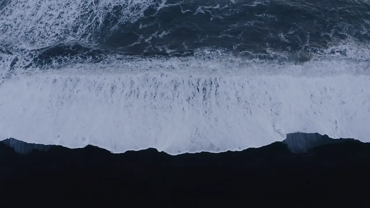 Fierce waves of the Atlantic hitting black sand beach in Iceland aerial straight down