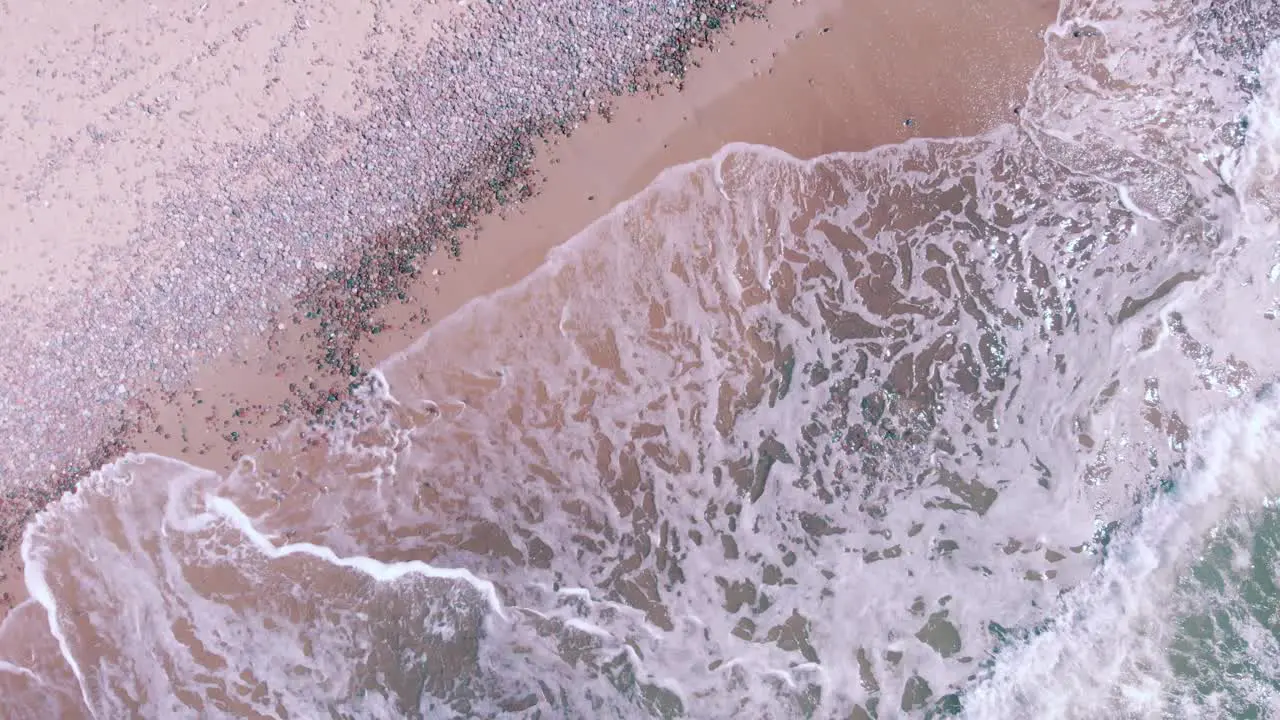 Drone aerial getting close to waves crashing on a tropical pink beach with no one around