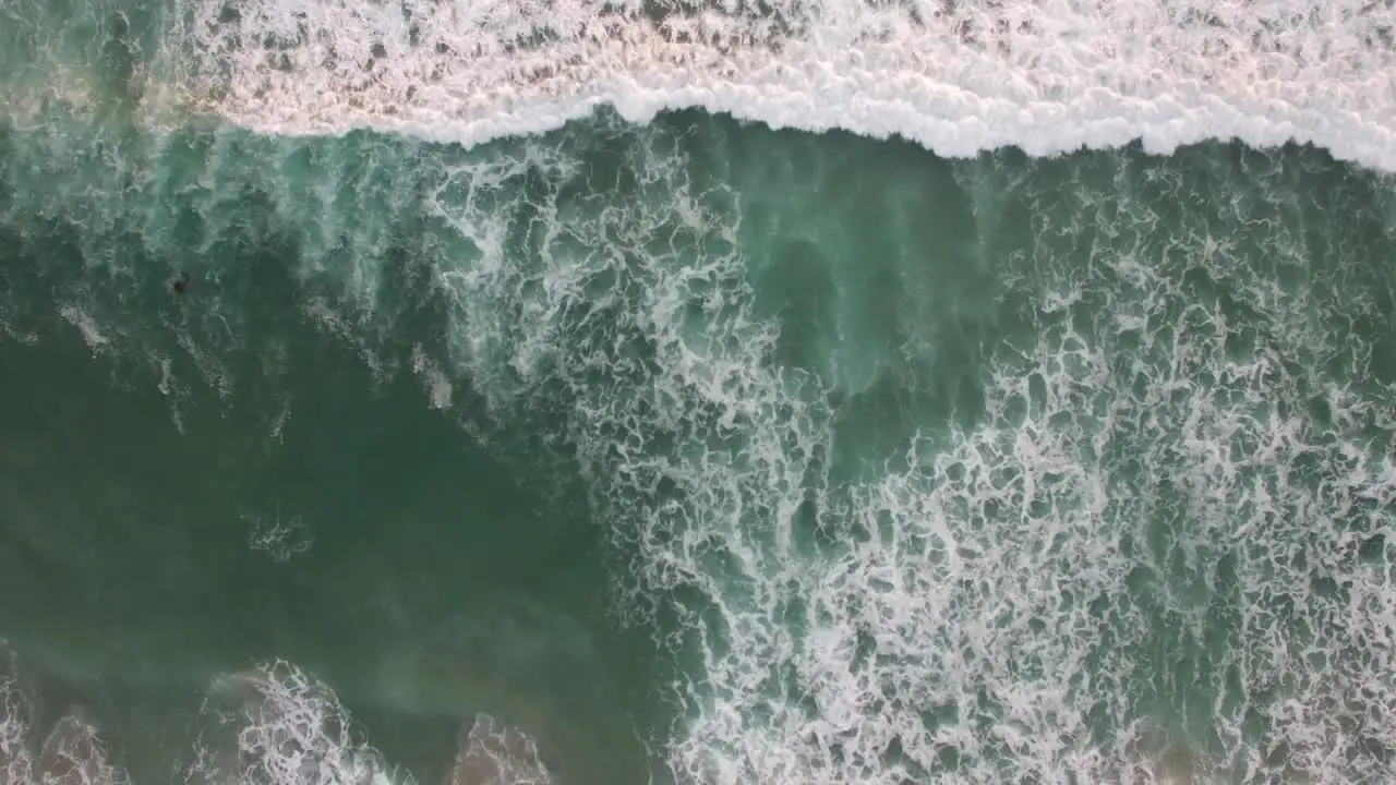 An aerial perspective looking straight down at the ocean with waves rolling in 1