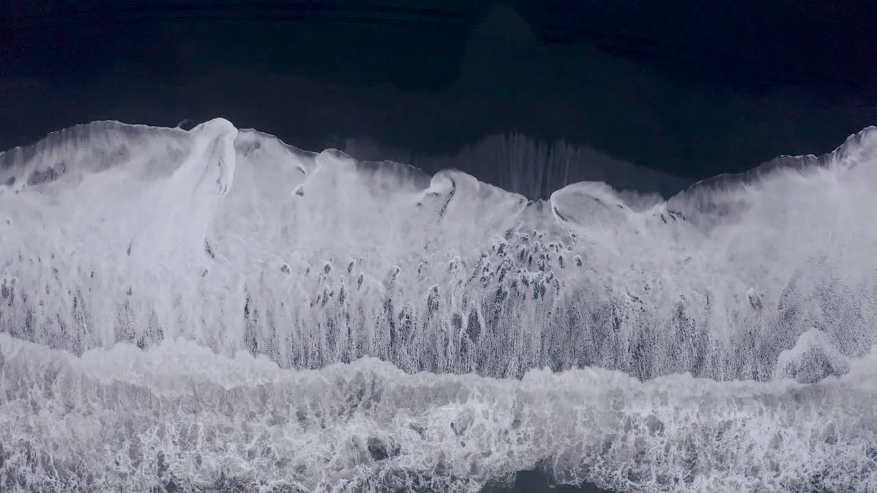 Aerial top down shot of giant ocean waves reaching black beach of Vi kurfjara Iceland