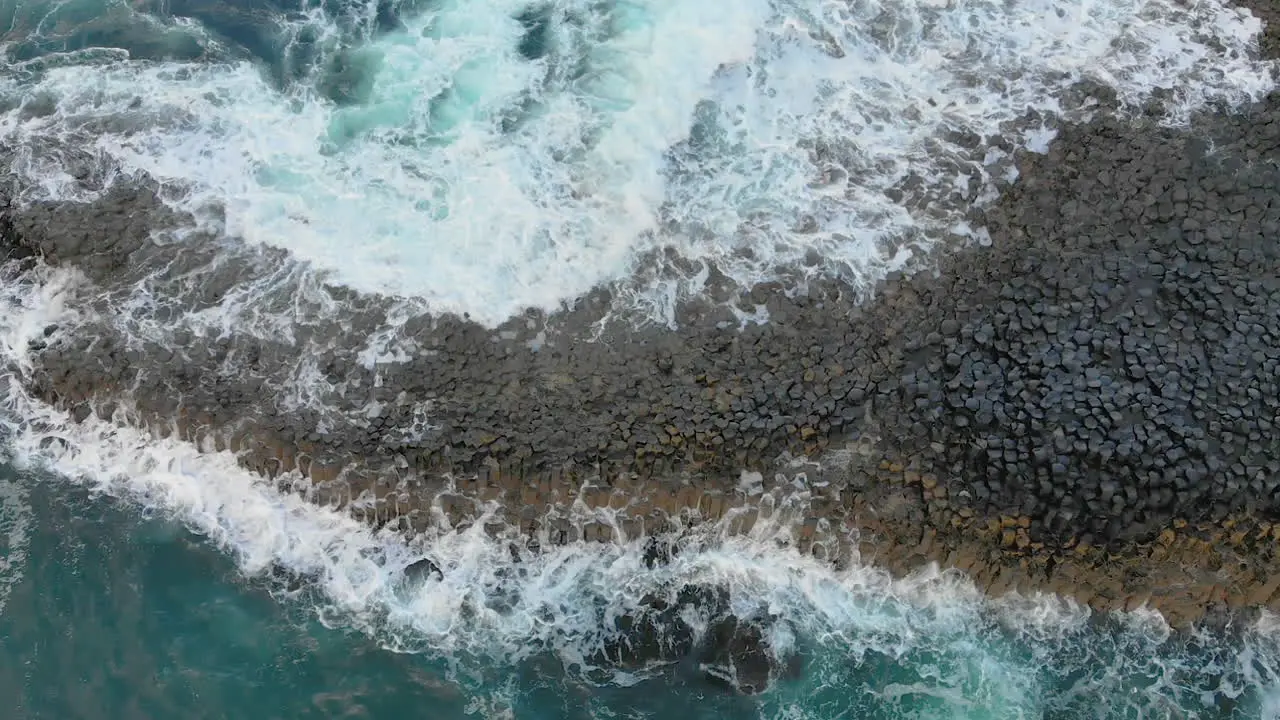 Static top down view of oceanic waves splashing at the shore's rock formation in Northern Ireland