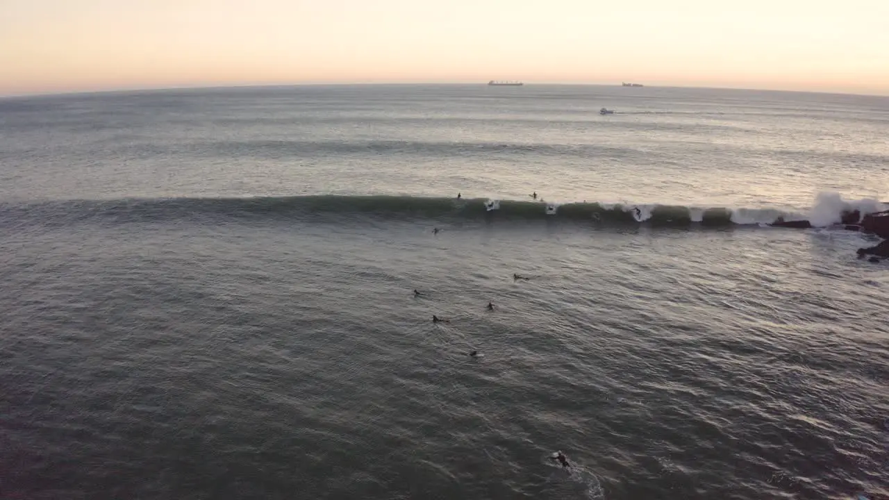 Aerial drone view following some surfers catching waves on coast of Portugal