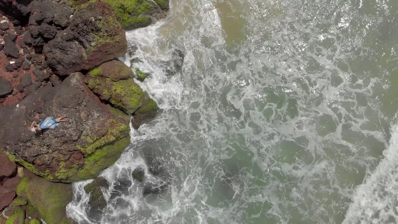 4k Aerial Top Down Drone Shot of a beautiful 27-year-old young Indian woman in White and Blue dress relaxing on top of a Cliff being crushed by the sea waves