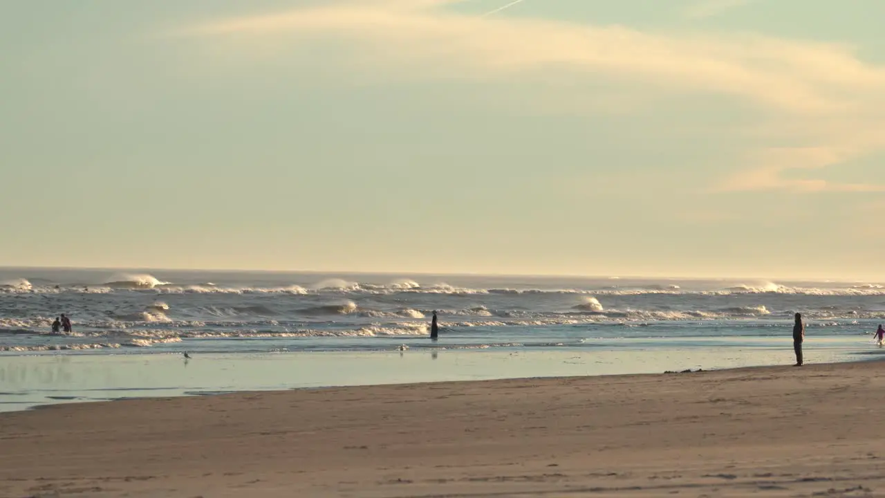 Tourist Silhouettes On Splashing Waves With Flock Of Sea Birds Landed On Coastline