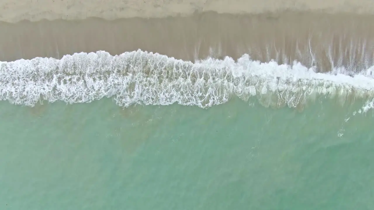 Looking down a calming view of crashing waves through the sandy seashore