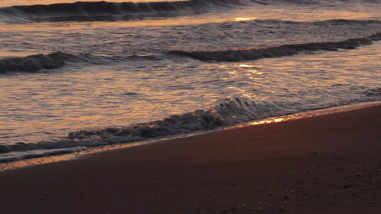 Sandy beach at sunrise with waves breaking on shoreline reflecting sunlight mediterranean sea close up spain