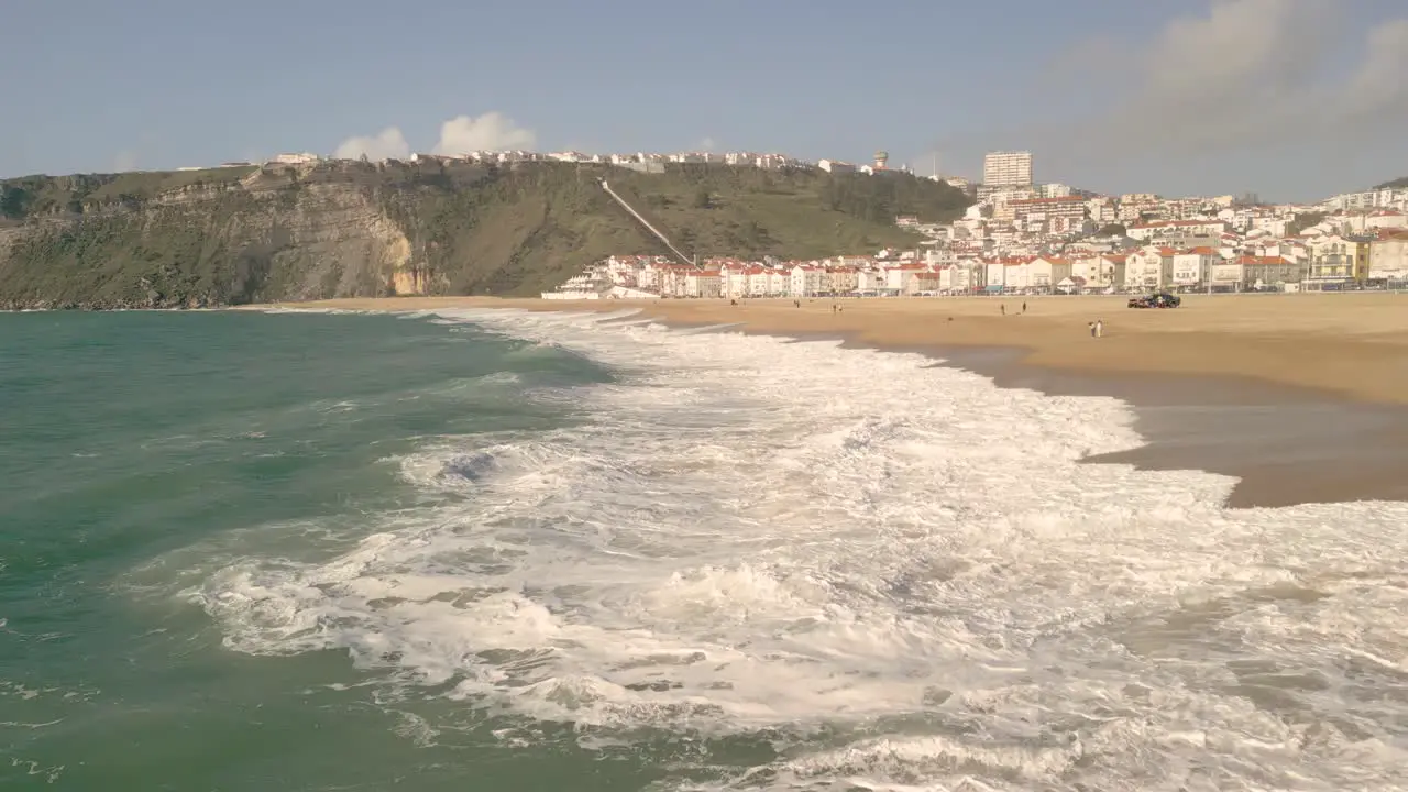 Big Waves Lapping On The Seashore During Summer Season And Suburb In Distance In Nazare Portugal