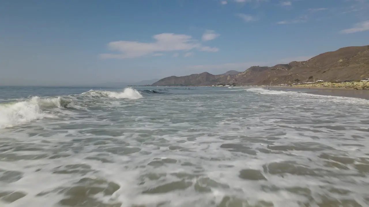 A drone shot skimming over waves and rising up over a group of surfers