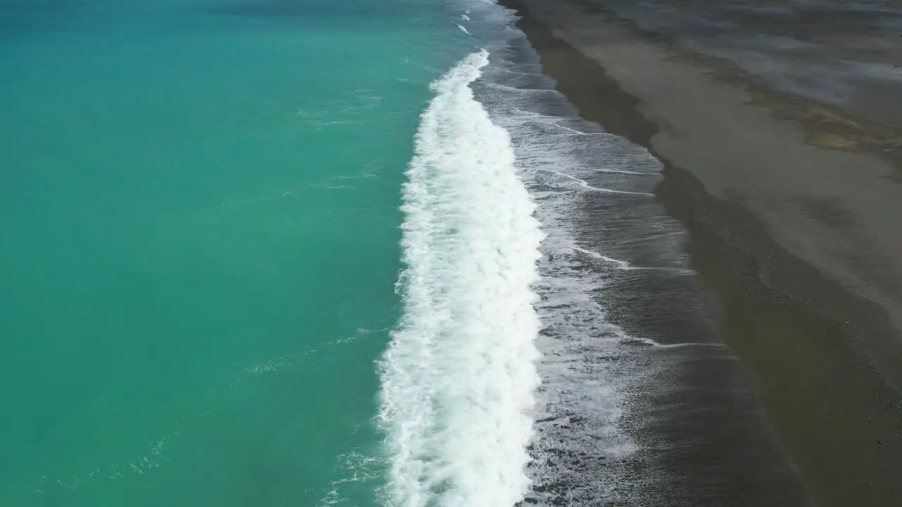 Aerial slow-motion over beautiful turquoise-colored South Pacific Ocean as white-water contrasts with dark stony shore Birdlings Flat Beach