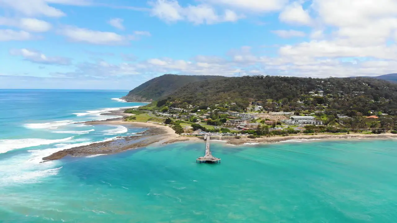 Aerial flying backward from the pier over the tropical aqua ocean