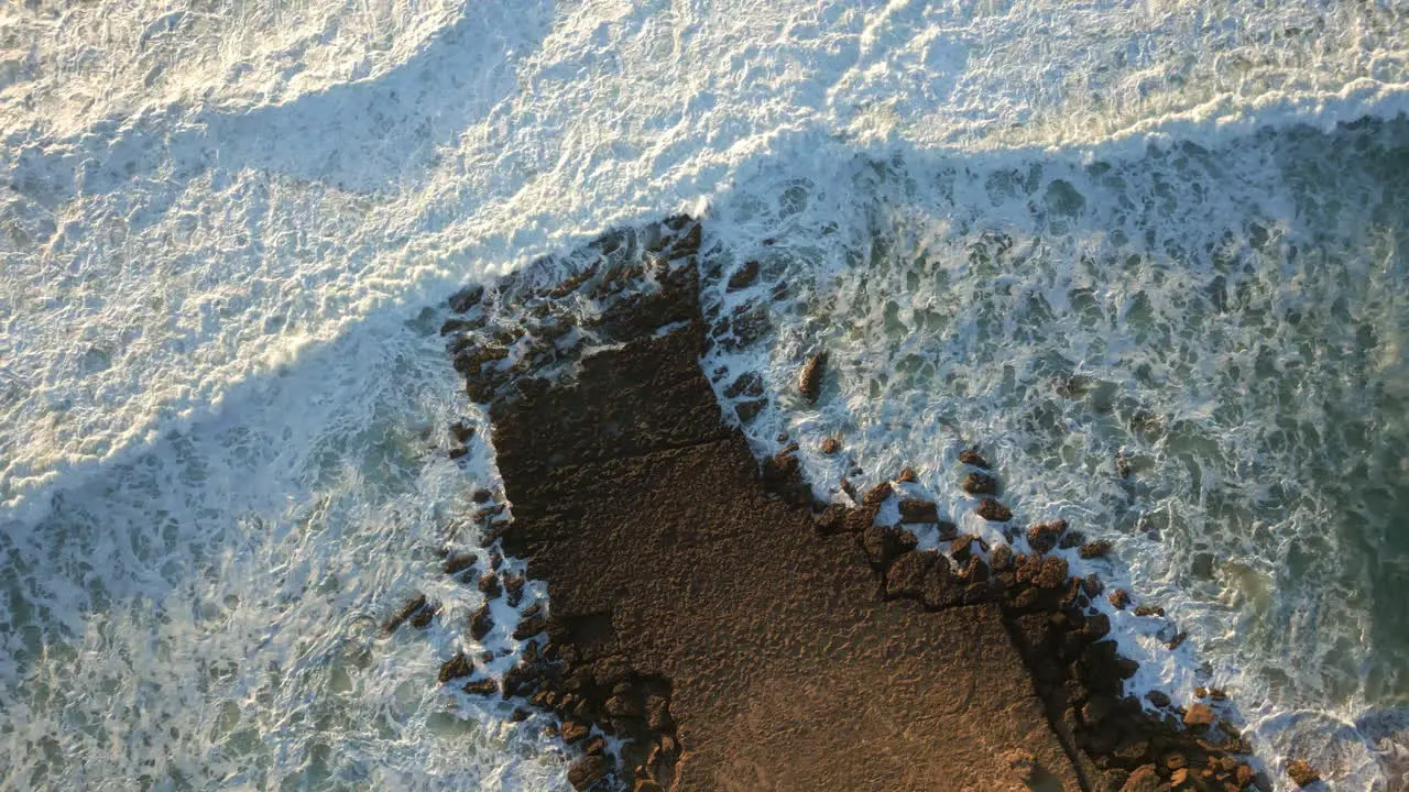 Top down drone shot over rocks and waves breaking