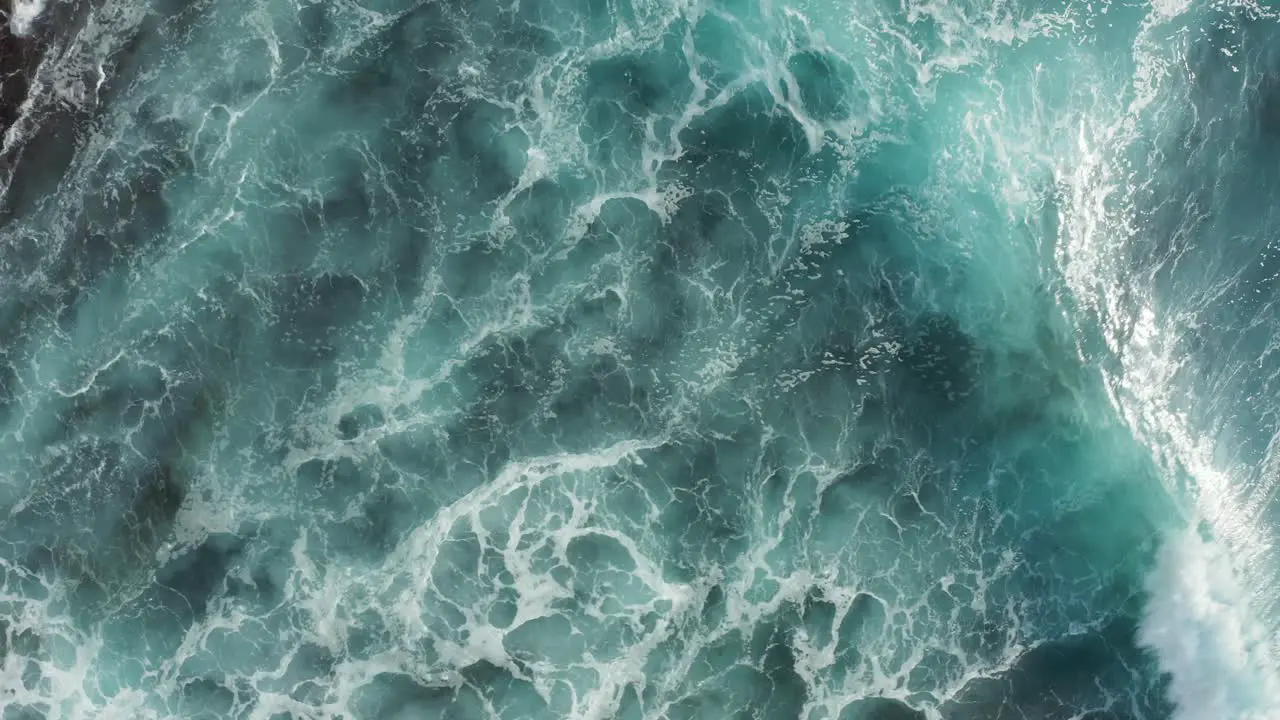 Beautiful aerial top down view of turquoise blue ocean waves crashing and rolling on top of coastline reef rocks