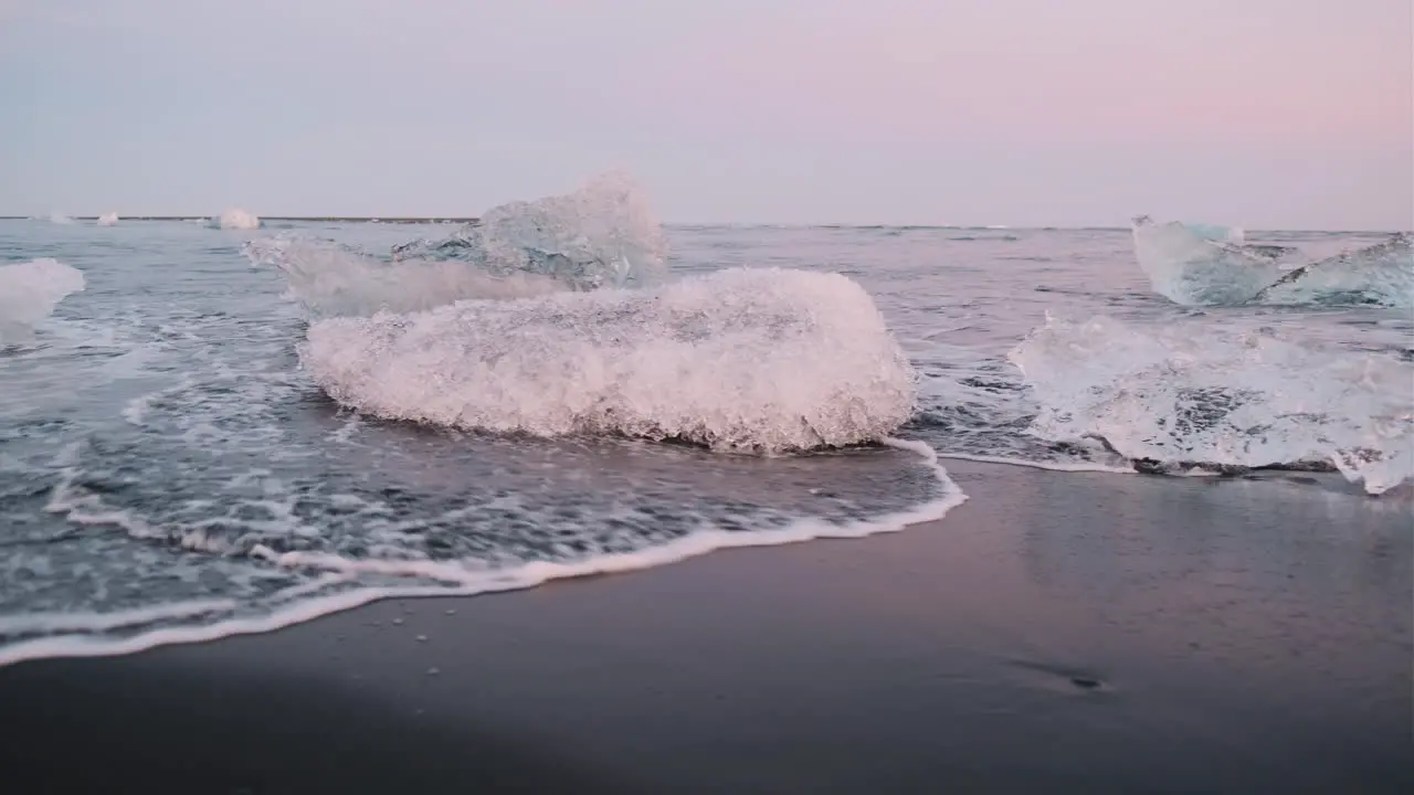 Handheld pan of waves washing around chunks of ice on Diamond Beach Iceland