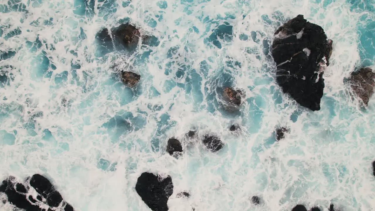 Top down view of waves crashing on rocky beach in Hawaii aerial pan left to right