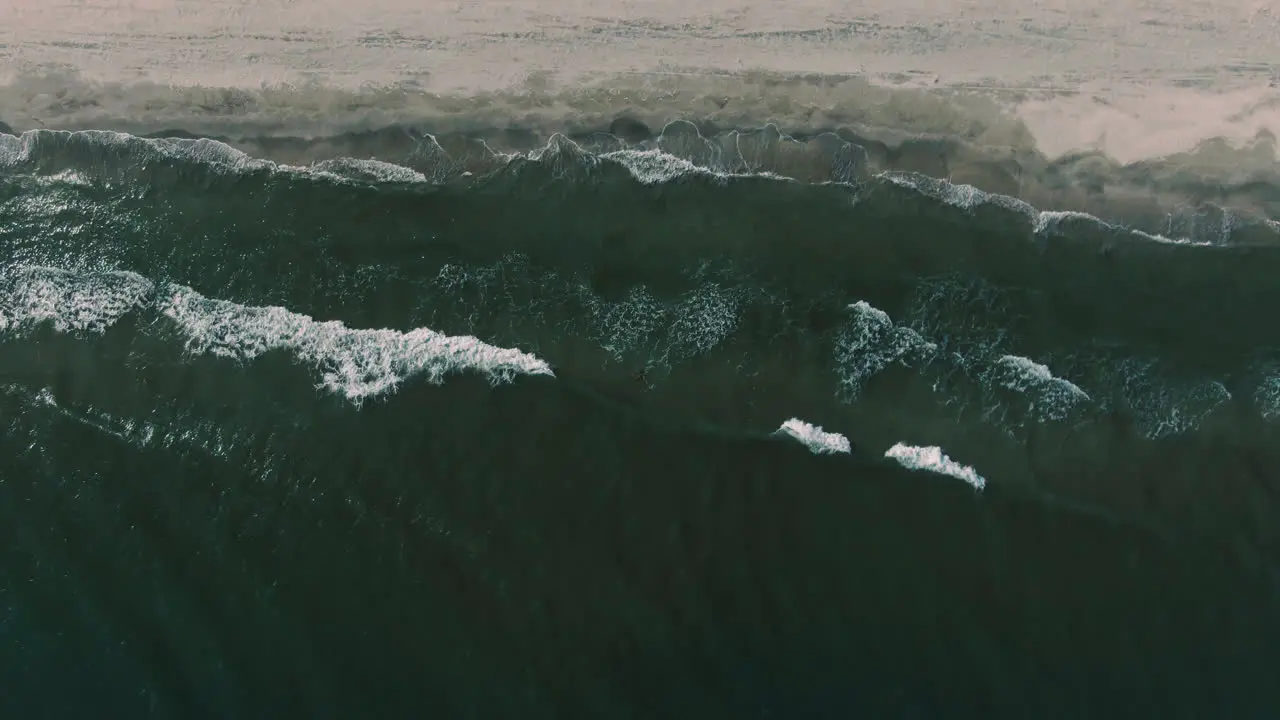 Ascending drone shot over the seashore with mesmerizing waves on a clear sunny day