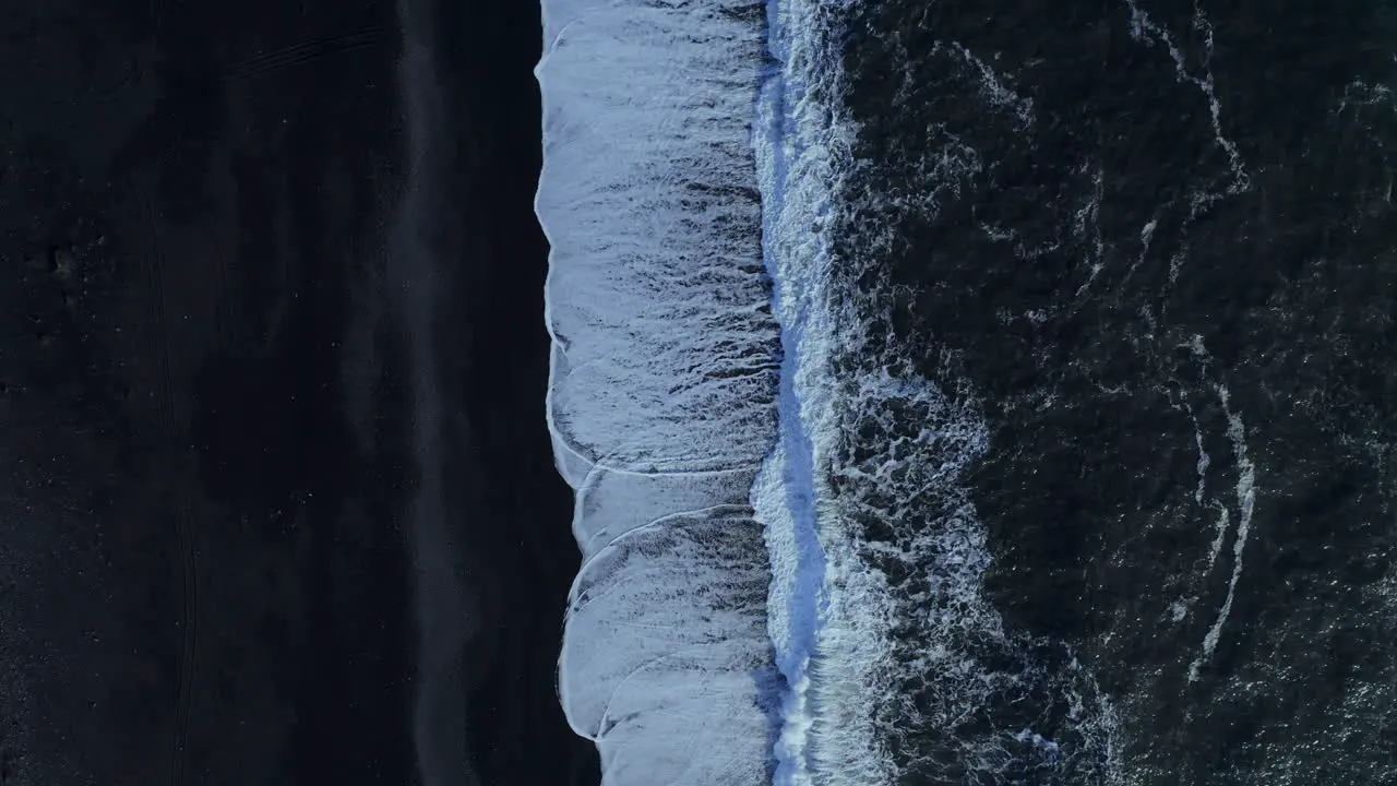 White surf waves rolling on black sand -top view