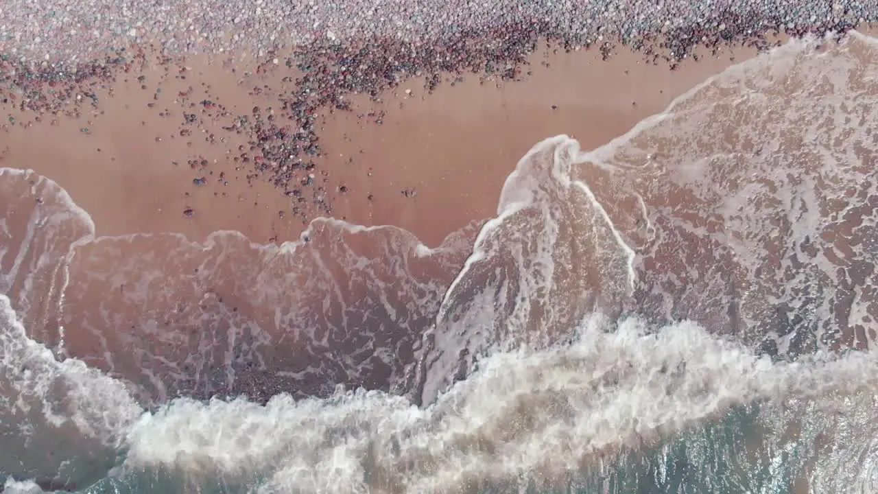 Ocean waves hitting sandy beach with small pebbles aerial top down view