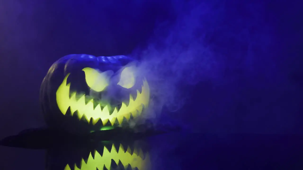 Video of halloween carved pumpkin with smoke and blue light on black background