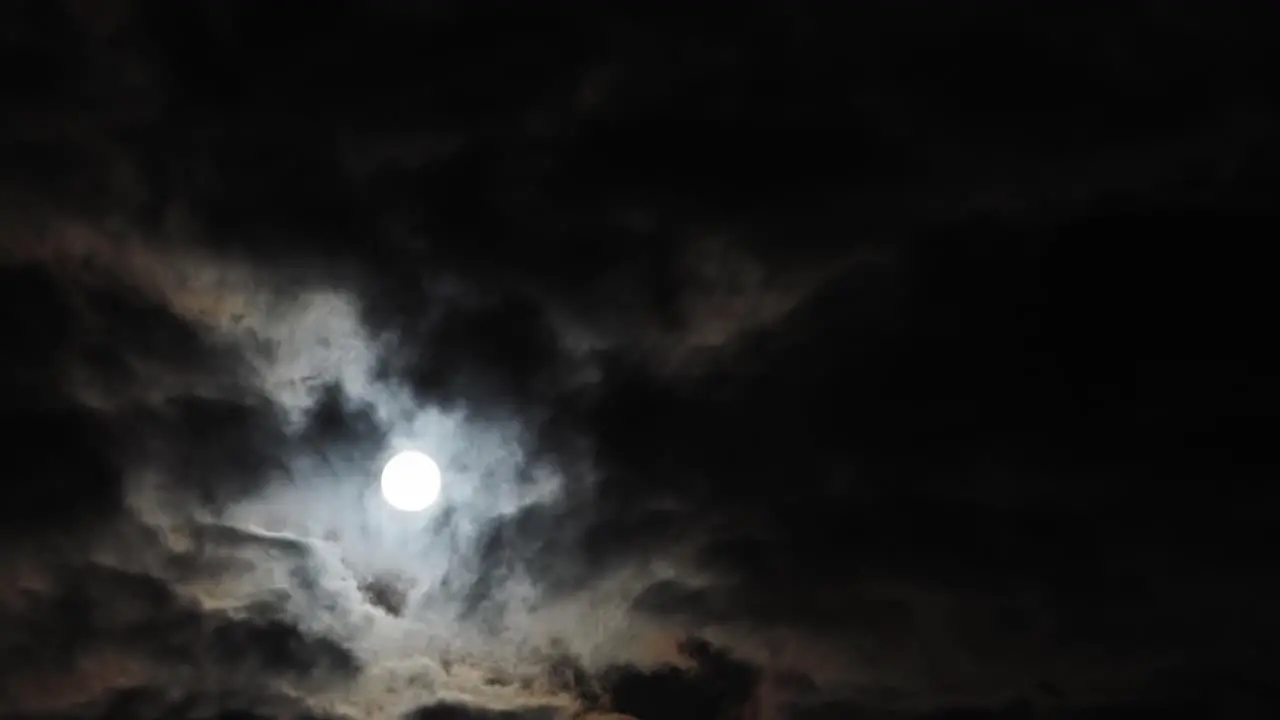 Slow timelapse of rising full moon behind broken clouds copy space