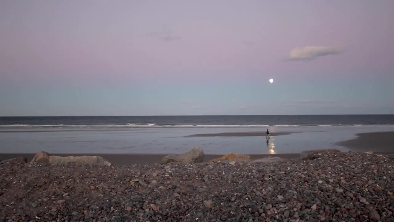 Moonrise over a beach on the Atlantic while a couple walks across the sand