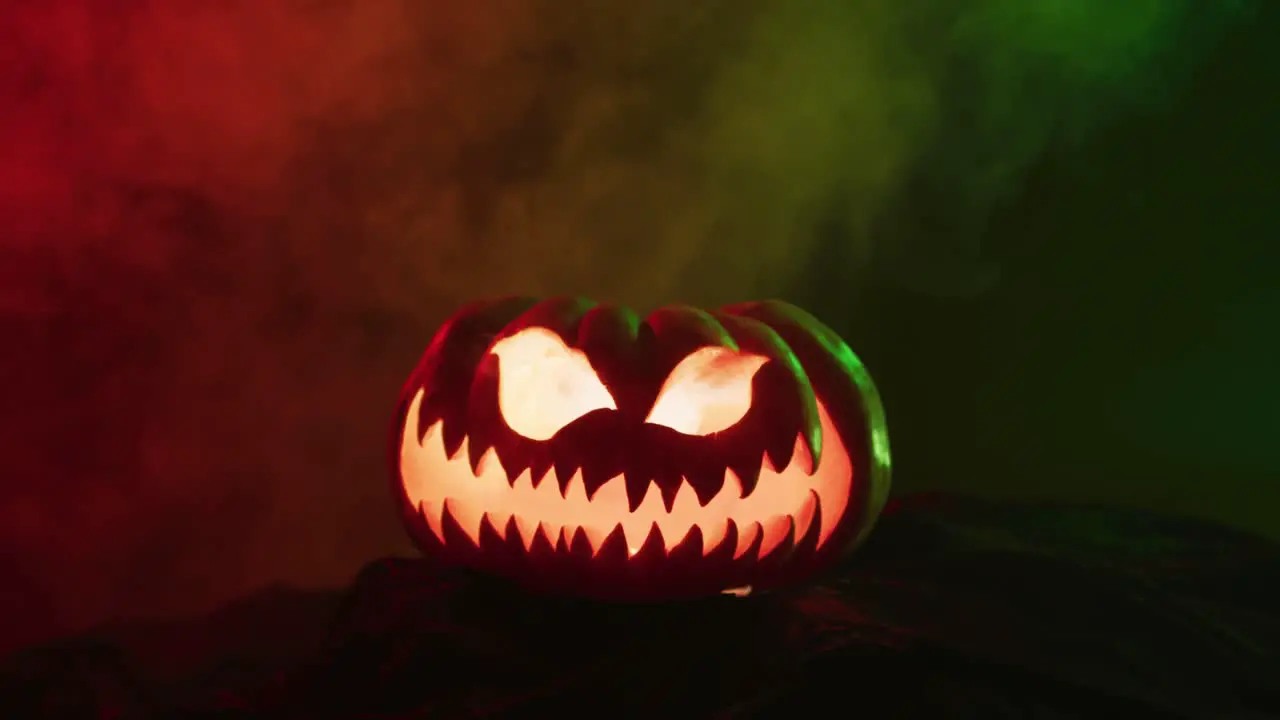 Video of halloween carved pumpkin with smoke and green and red light on black background