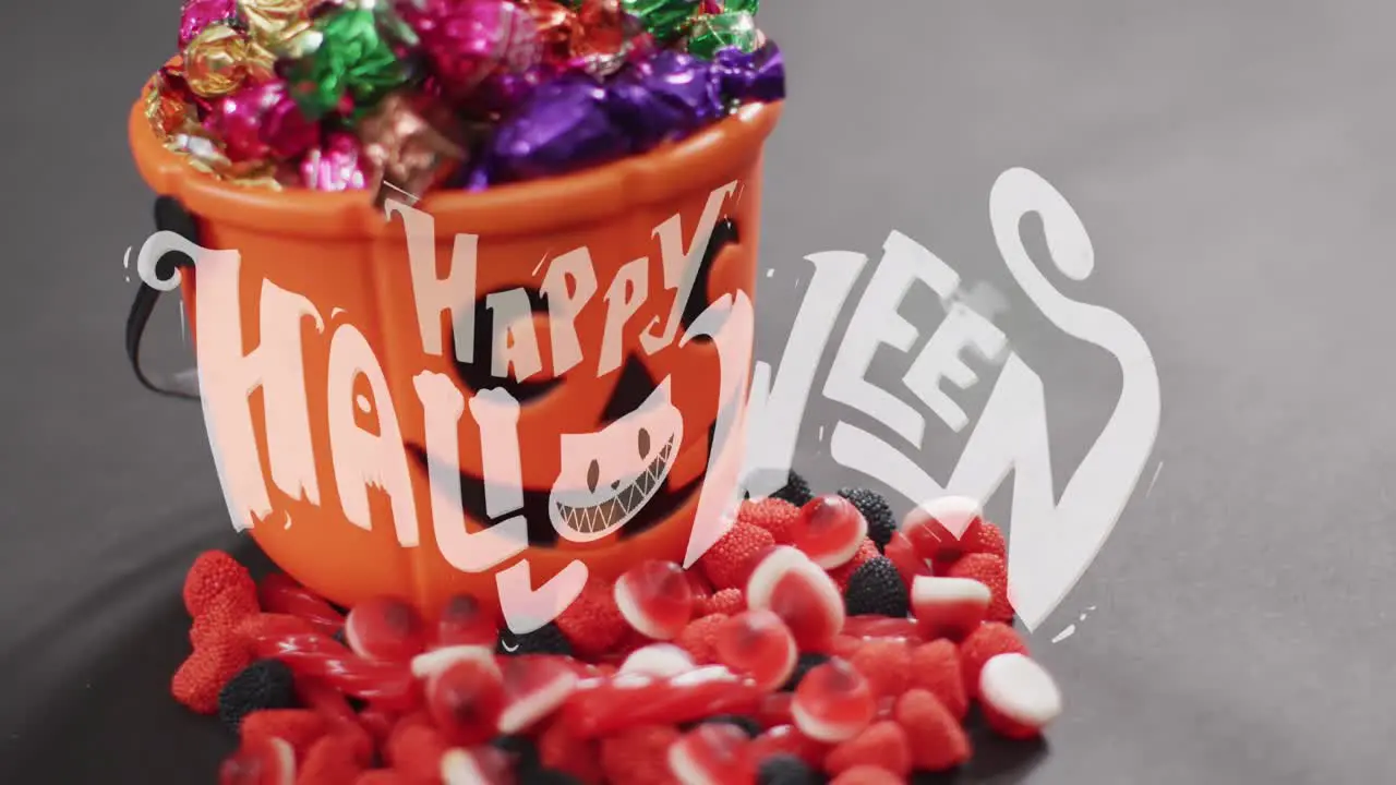 Animation of happy halloween text over pumpkin bucket and sweets