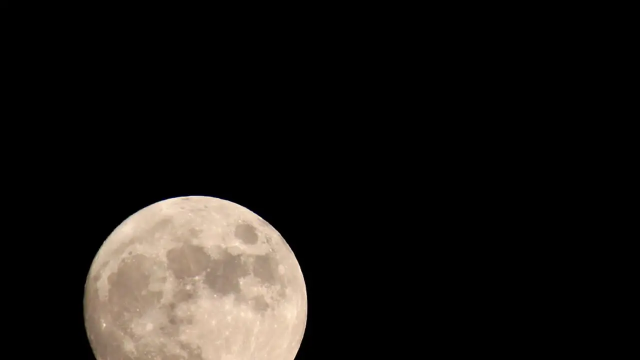 Starting with only the top third of a bright yellow orange full moon visible moon moves fully into the frame towards the center