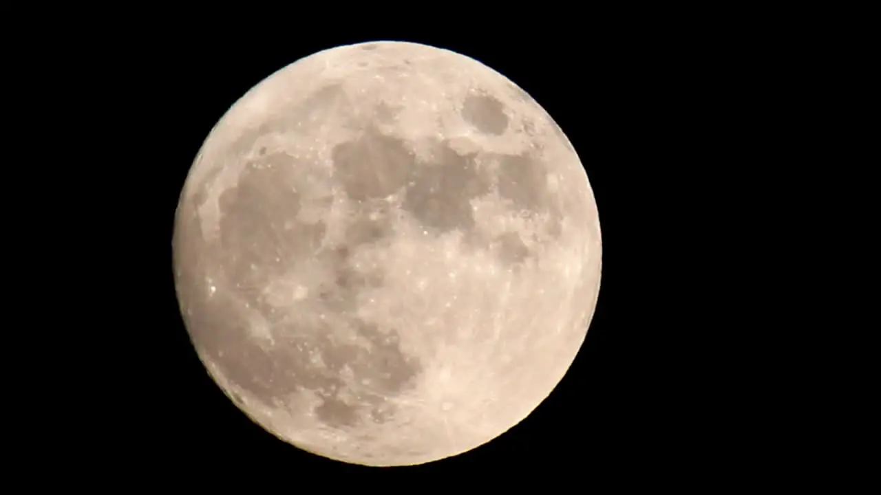 Zoomed into a bright yellow orange full moon that fills the frame zooming out until the moon is in the center of the frame offset slightly to the left