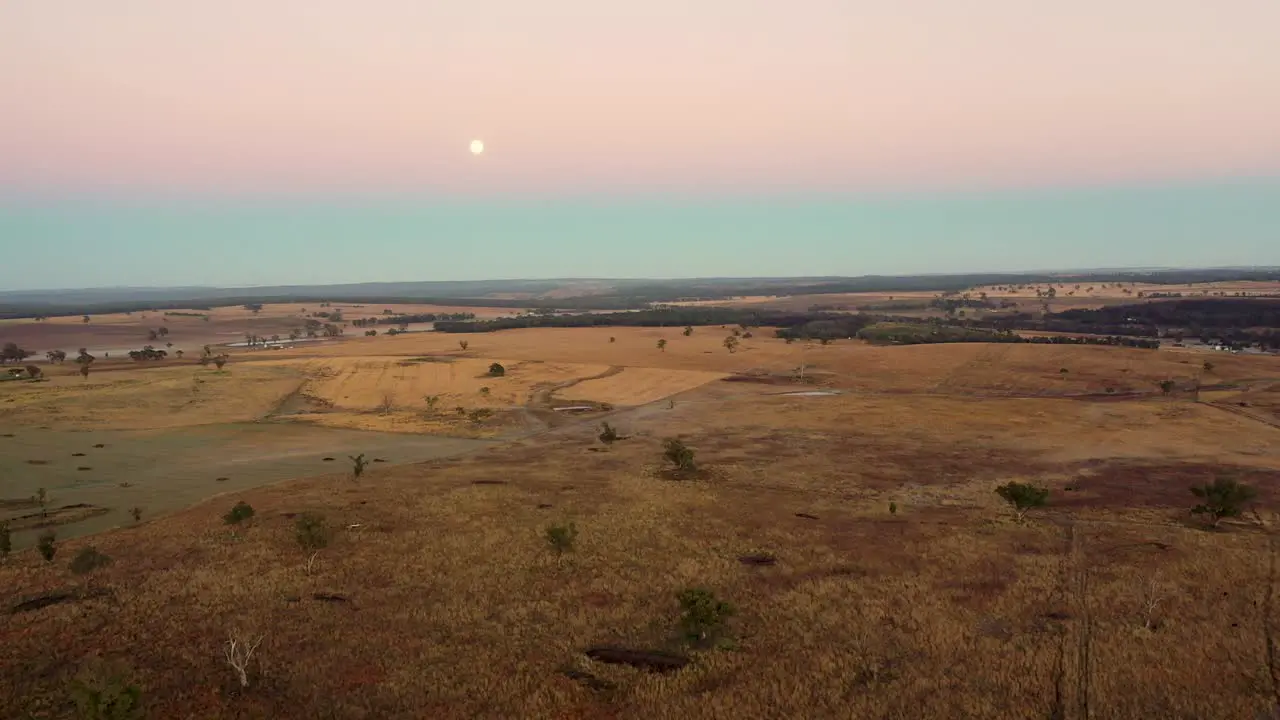 Early daytime Full moon over stretched brownish-yellow grassy plains aerial view