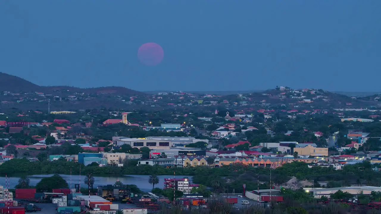 Deep blood red full blue supermoon rises above curacao container terminal in willemstad