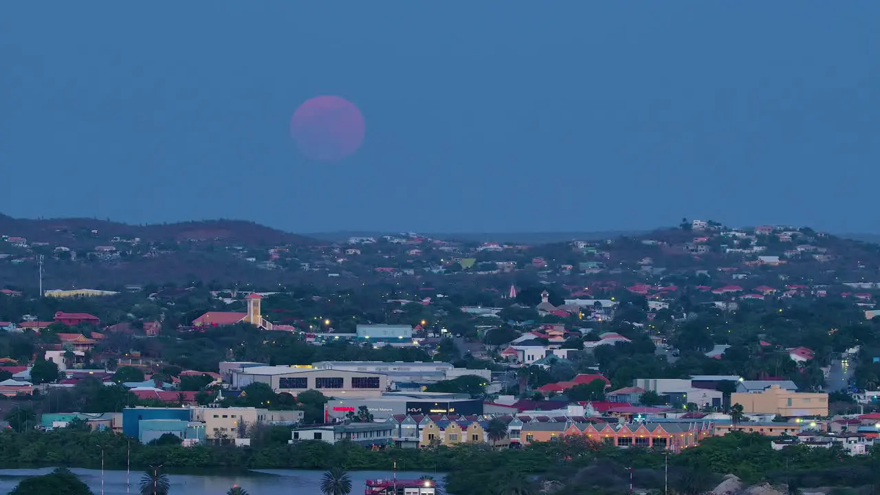 Slow zoom in as red purple supermoon rises slowly above willemstad curacao