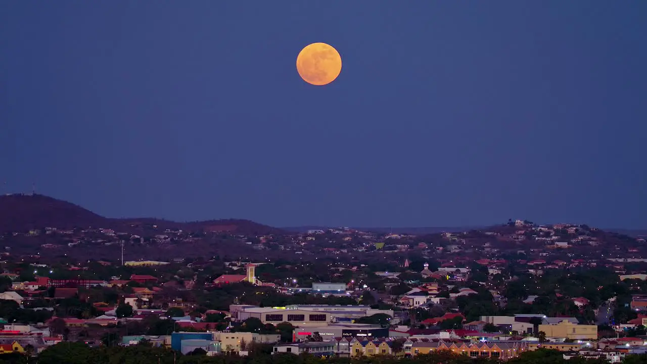 Pan up across curacao container industrial port zone terminal to red orange supermoon above city of willemstad