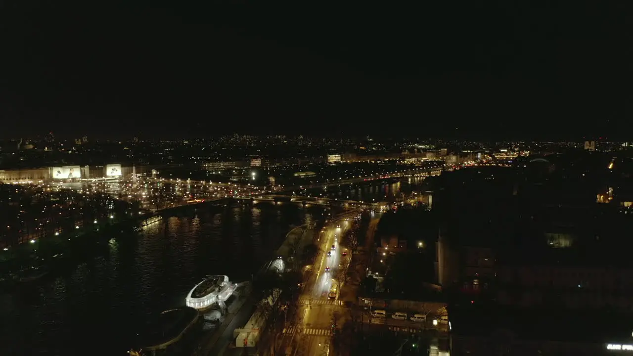 Forwards fly above busy Seine River waterfront at night Heading towards illuminated Place de la Concorde Paris France