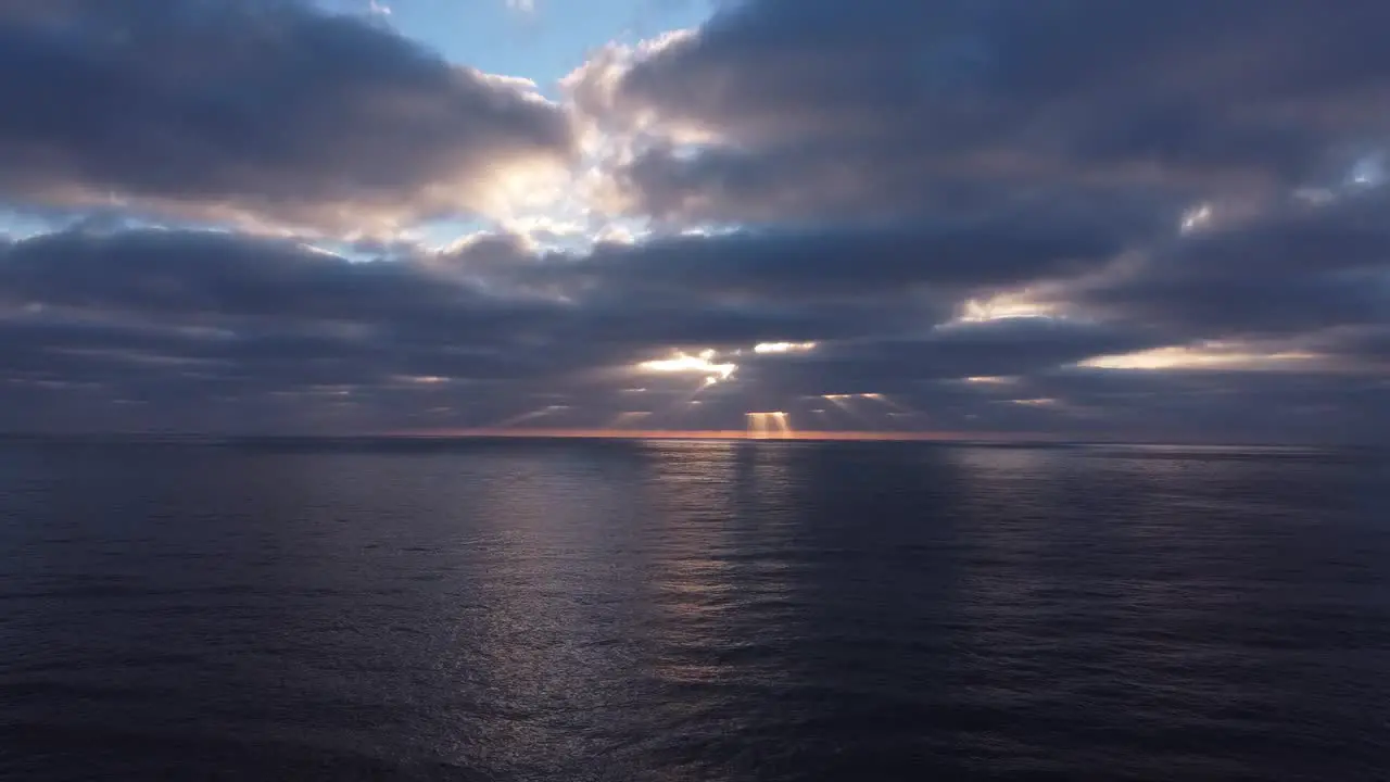 Drone view of sun rays peaking through thick dark clouds over the ocean in the evening