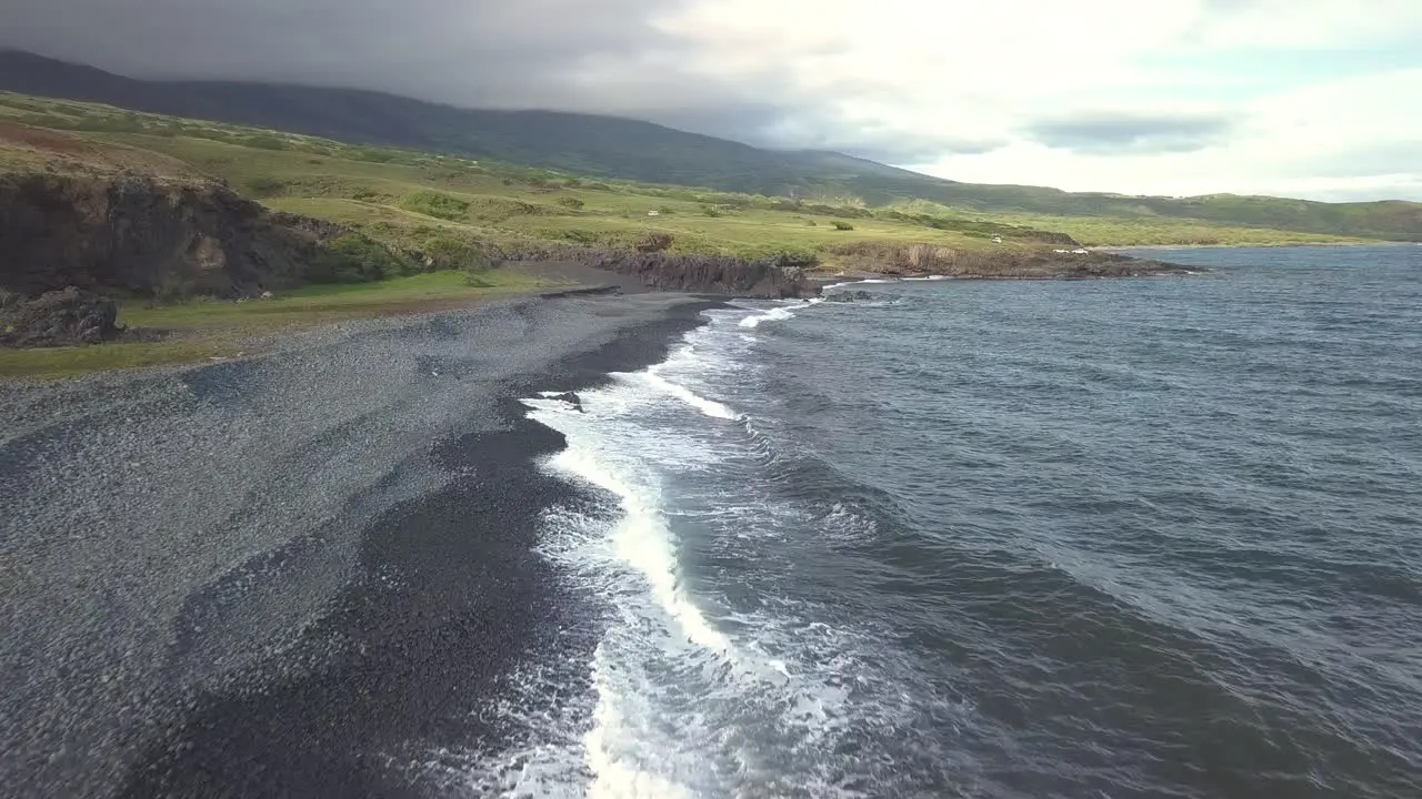 Waves crash ashore along the black coastline