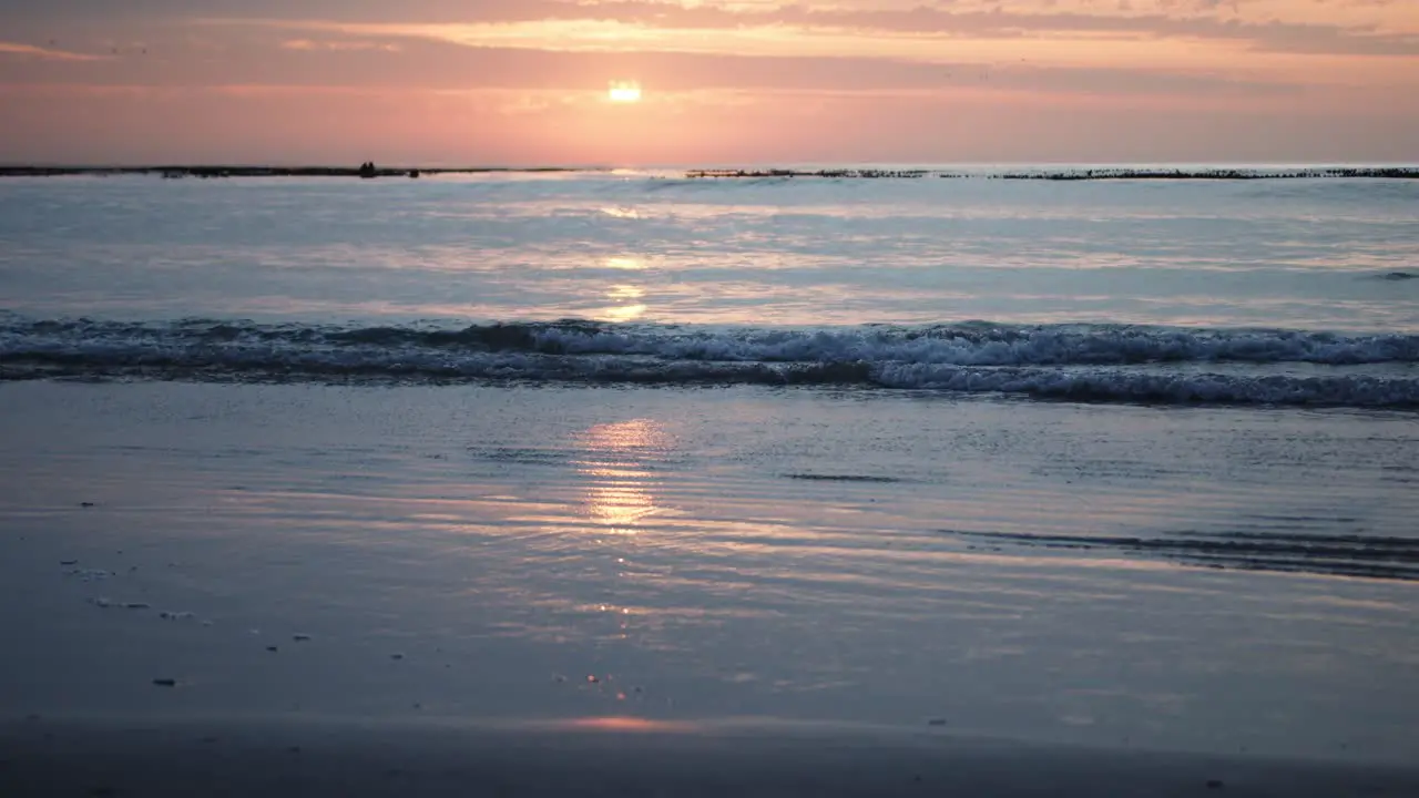 Sunrise reflects on waves as they come onto a tranquil beach in slow-motion