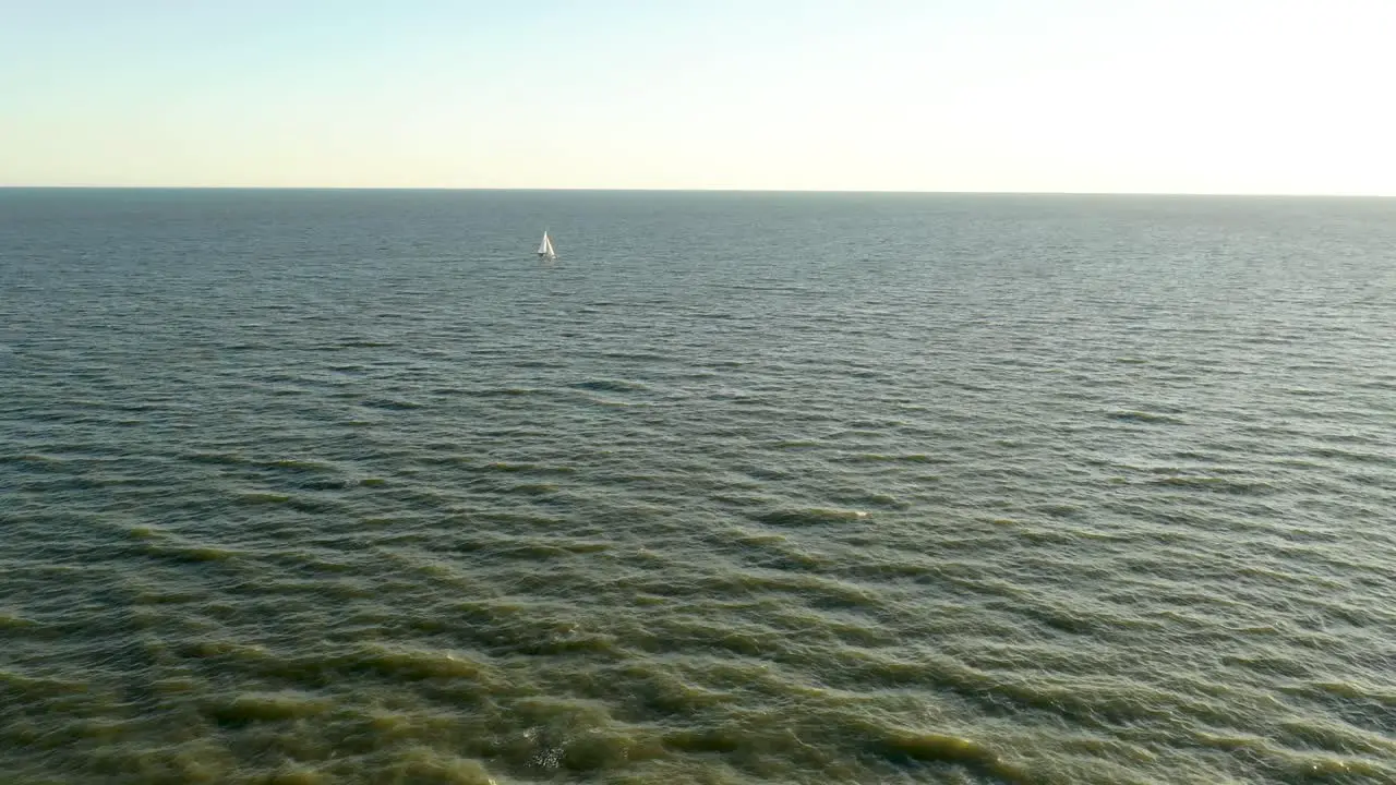 Aerial view of a sailboat in the distance sailing across the ocean