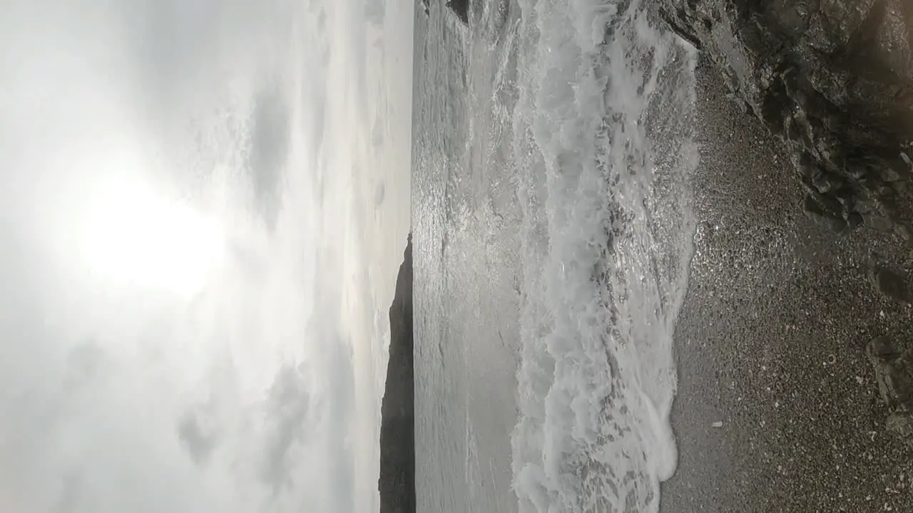 VERTICAL slow motion ocean waves crashing against rock coastline tranquil scene at sunrise