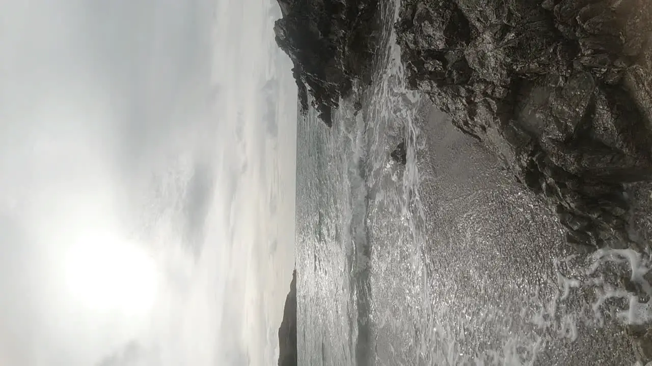 VERTICAL slow motion ocean waves crashing against rock sandy beach coastline at sunrise