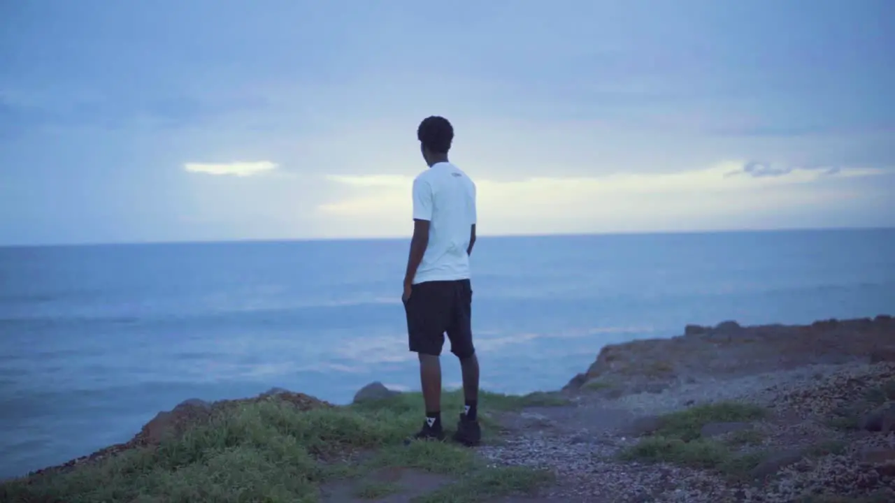 Young black man standing on a cliff looking at the sunset and the ocean