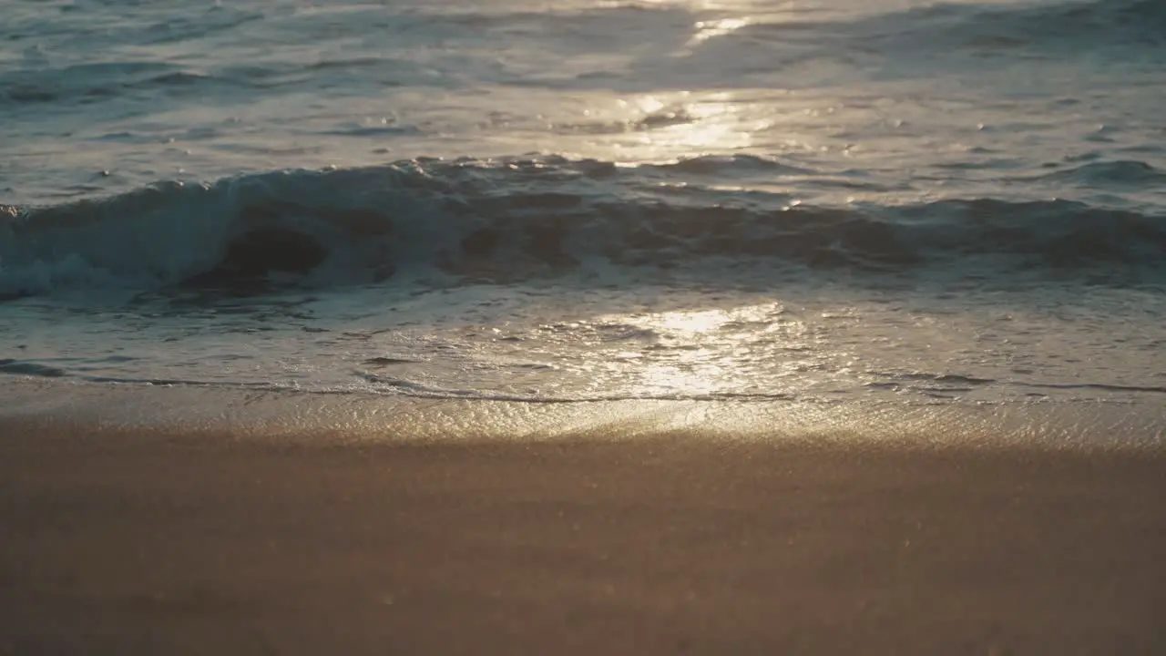 Small waves from the Pacific Ocean roll out onto a beautiful brown sand beach as the setting sun settles on the water