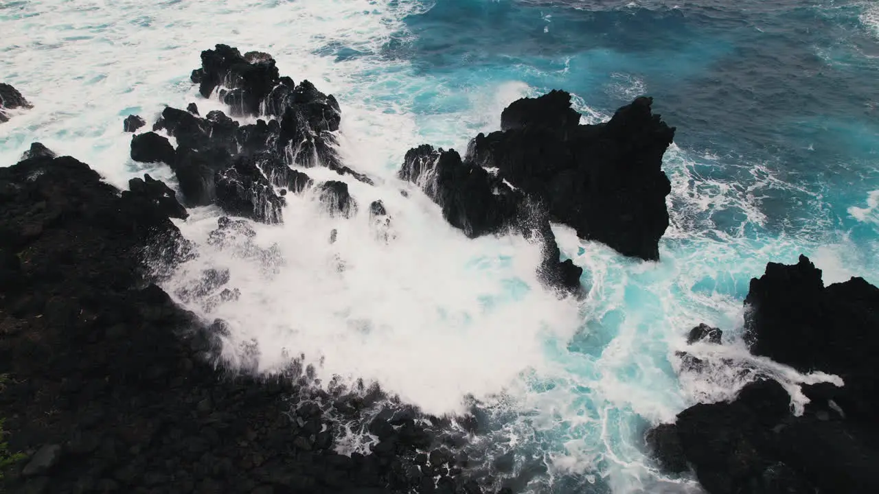 Slow motion aerial shot of powerful wave crashing over jagged lava rocks in Hawaii