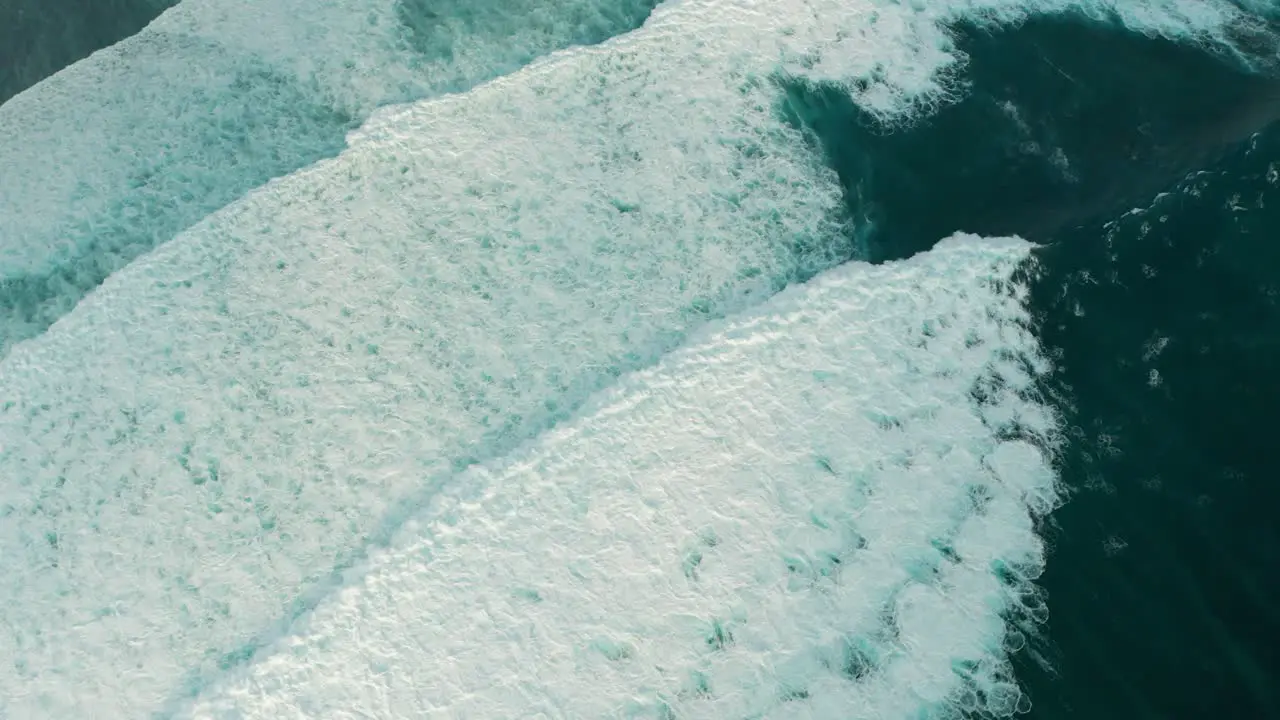 Whitewater waves roll towards shore seen from above aerial