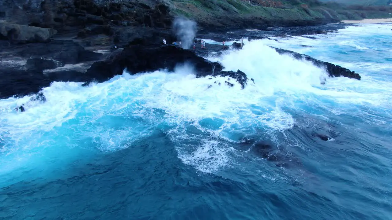 Halona blowhole in hawaii shooting up on a stormy day as waves break and tourists watch